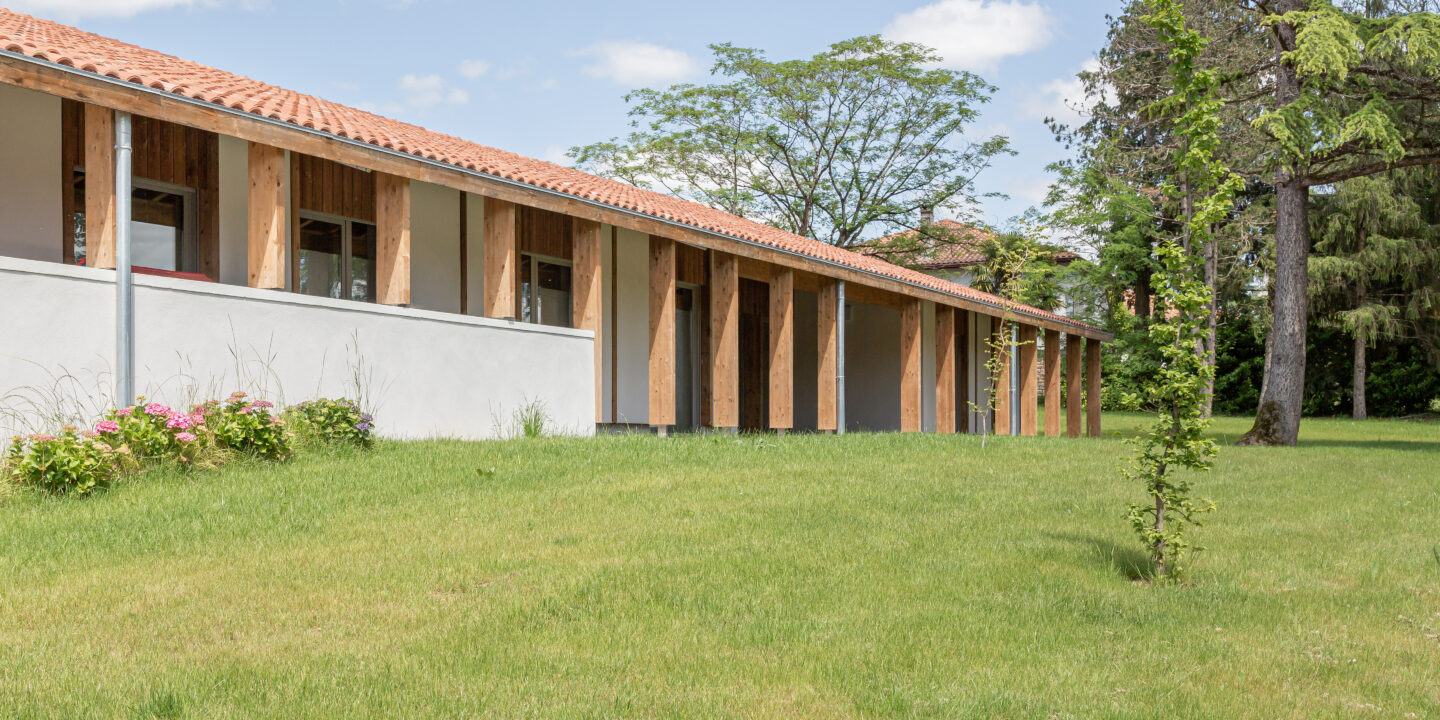 Façade de la Maison de Santé AMIKUZE avec galerie couverte en bois ouverte sur les espaces verts.