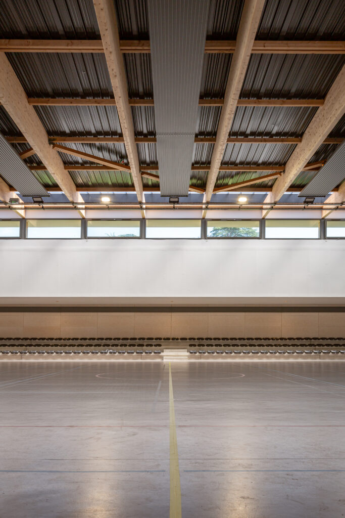 Vue intérieure du gymnase mettant en valeur la structure bois, les gradins et le terrain de sport.