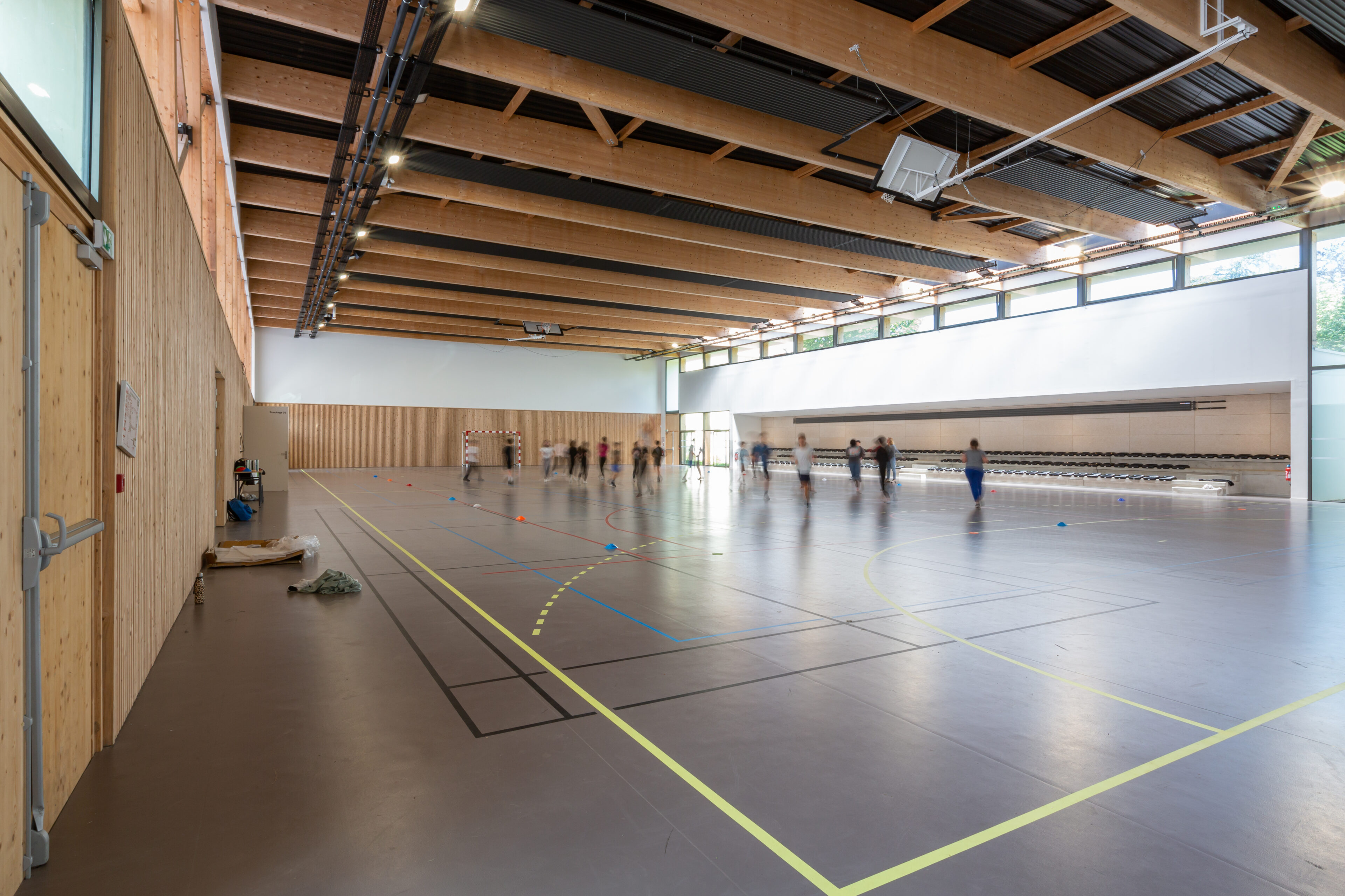 Grand volume intérieur du gymnase du groupe scolaire Largenté à Bayonne avec charpente en bois lamellé et équipements sportifs.