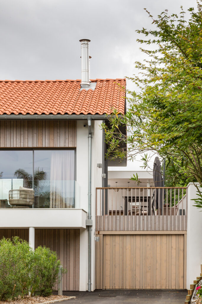 Façade principale d'une villa rénovée à Anglet, mêlant enduit blanc, bois naturel et grandes baies vitrées.