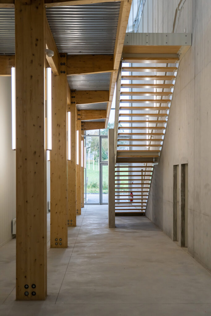 Hall d'accueil avec structure bois apparente et escalier contemporain dans la pépinière agroalimentaire.
