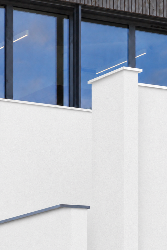 Détail architectural de la façade de l'atelier Castel mêlant bardage bois, enduit blanc et ouvertures encadrées.