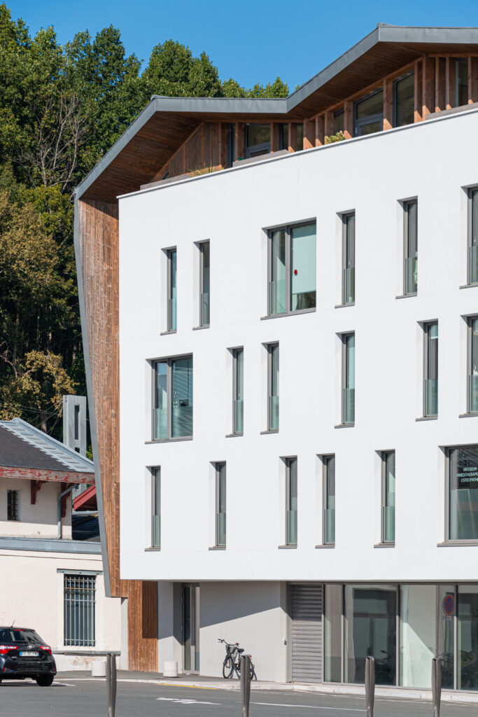 Architecture contemporaine d'un immeuble mixte de santé à Bayonne avec façades enduites blanches et attique en bois.