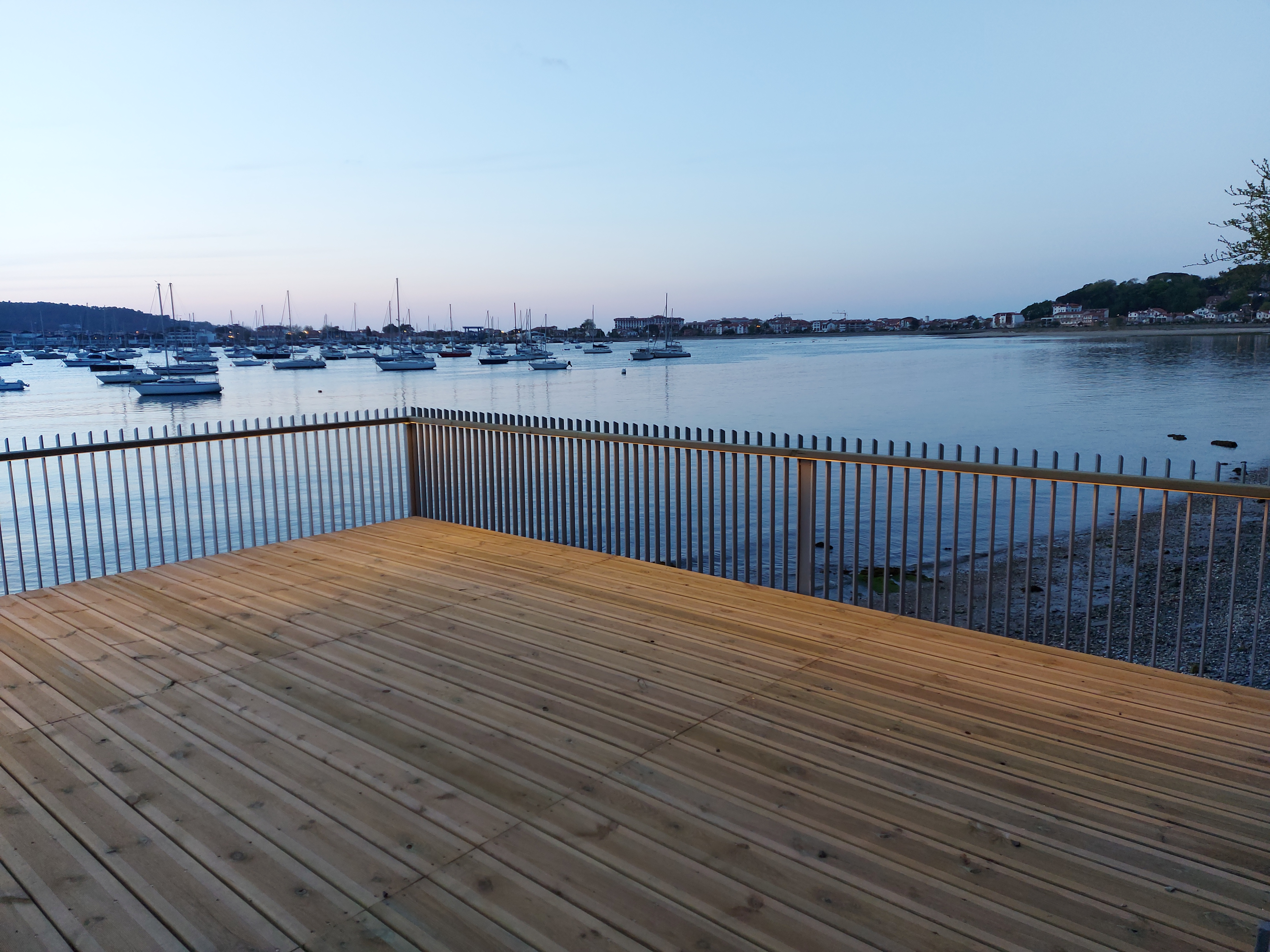 Passerelle piétonne en bois et métal de nuit, éclairage intégré, vue sur la baie d'Hendaye et ses bateaux au mouillage.