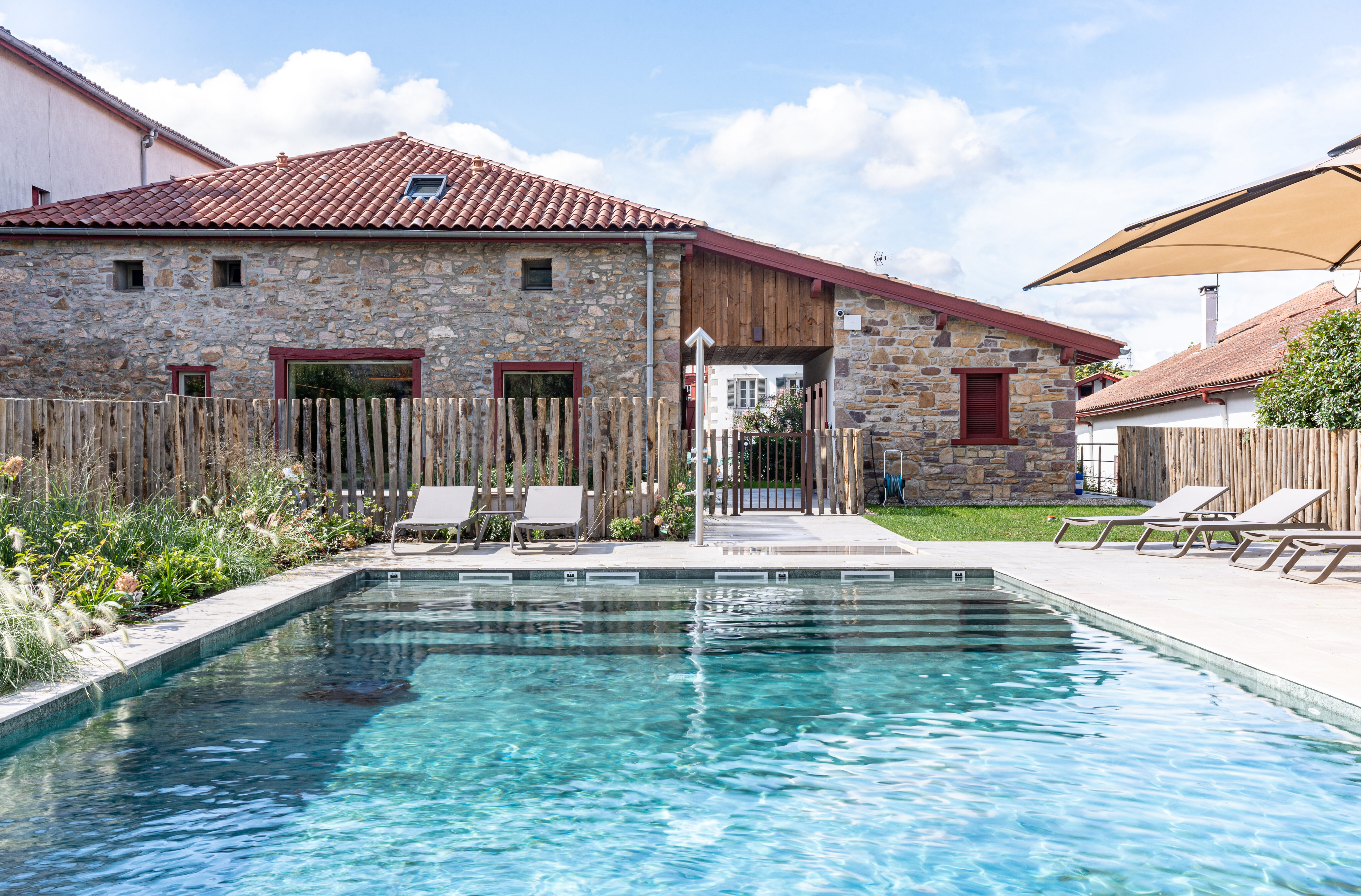 Bâtiment en pierre du spa Oppoca avec toiture en tuiles, clôture en bois et piscine extérieure en pierre naturelle verte.