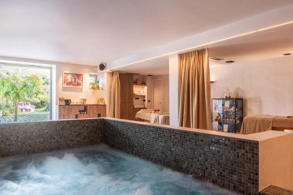 Intérieur du spa Oppoca, bassin à remous carrelé en mosaïque, espace de soins et vue sur le jardin basque.