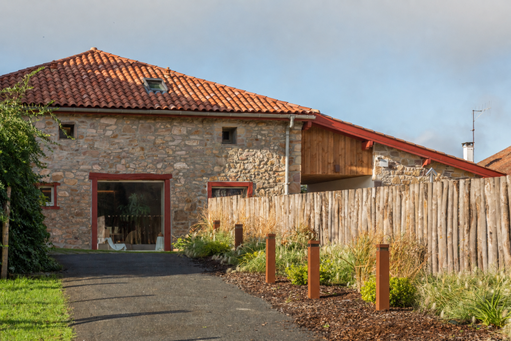 Vue du spa Oppoca depuis le jardin, façade en pierre et charpente bois apparente sous ciel couvert.