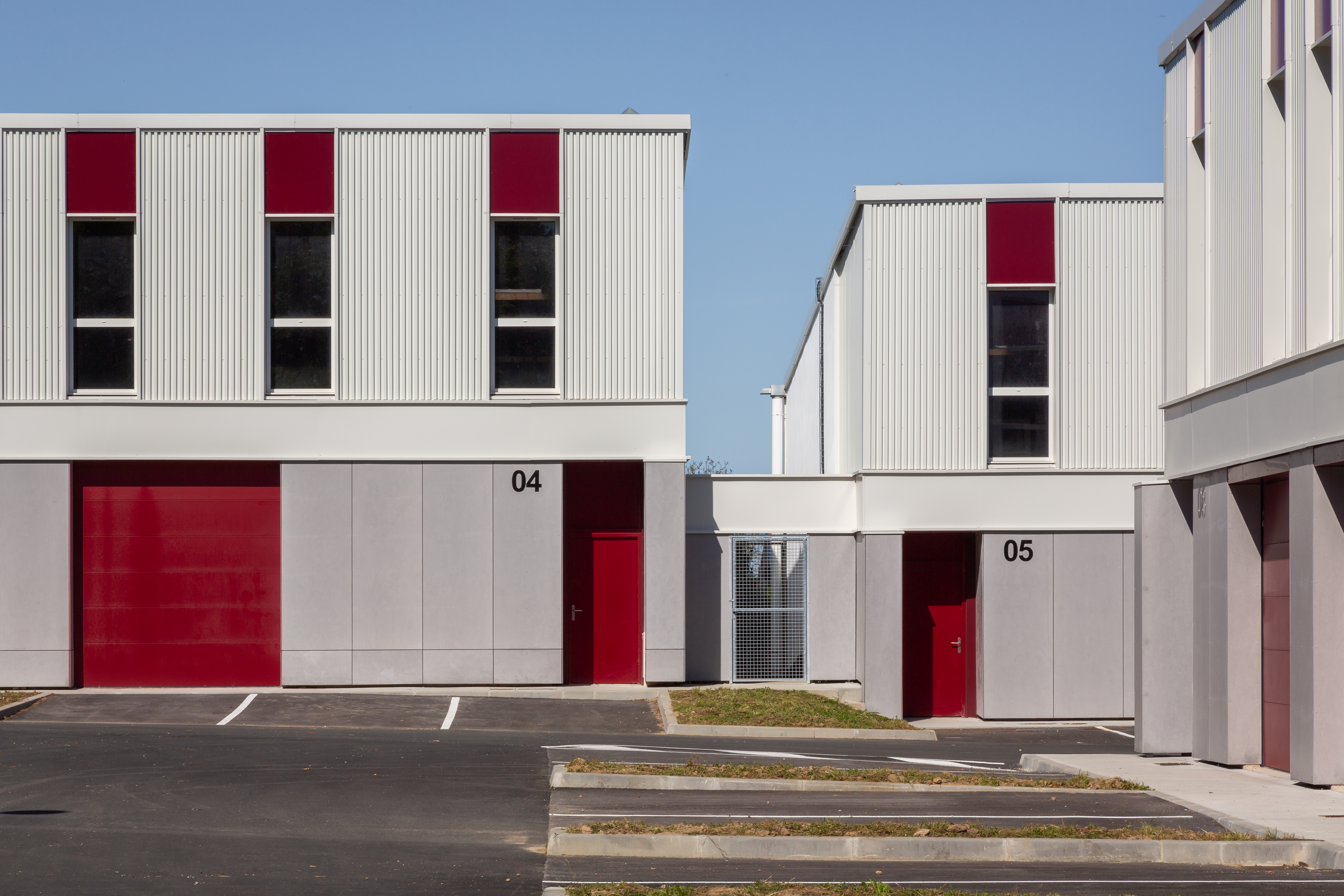 Façade sur cour du village d'artisans Etxondo, modules à ossature métallique gris clair, portes sectionnelles rouge bordeaux